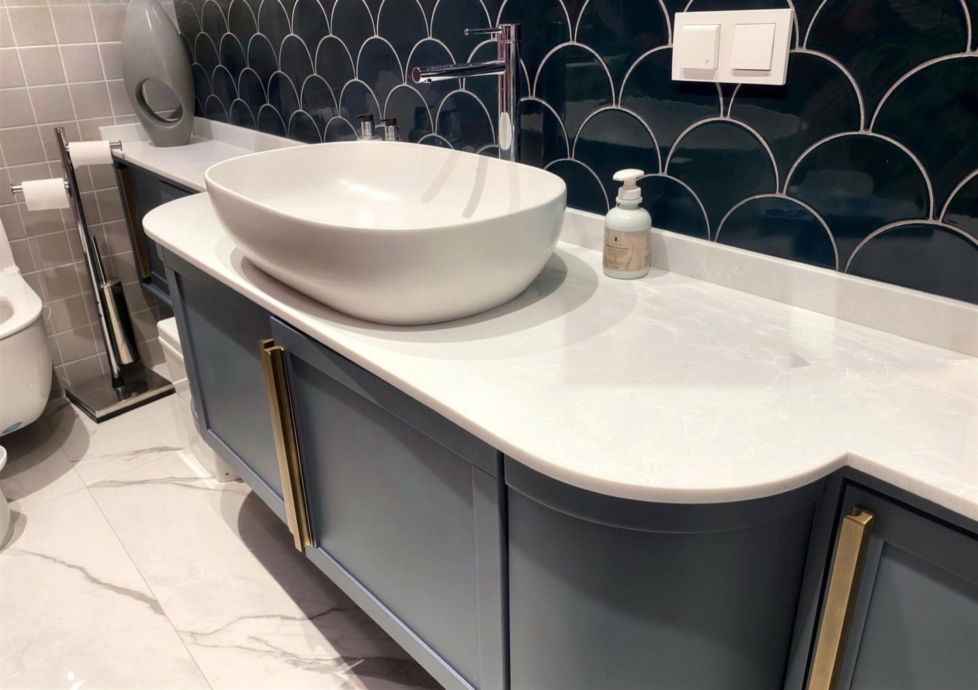 Gri-mavi lake kavisli gövdeli banyo dolabı, beyaz tezgâh, çanak lavabo ve pirinç kulplar